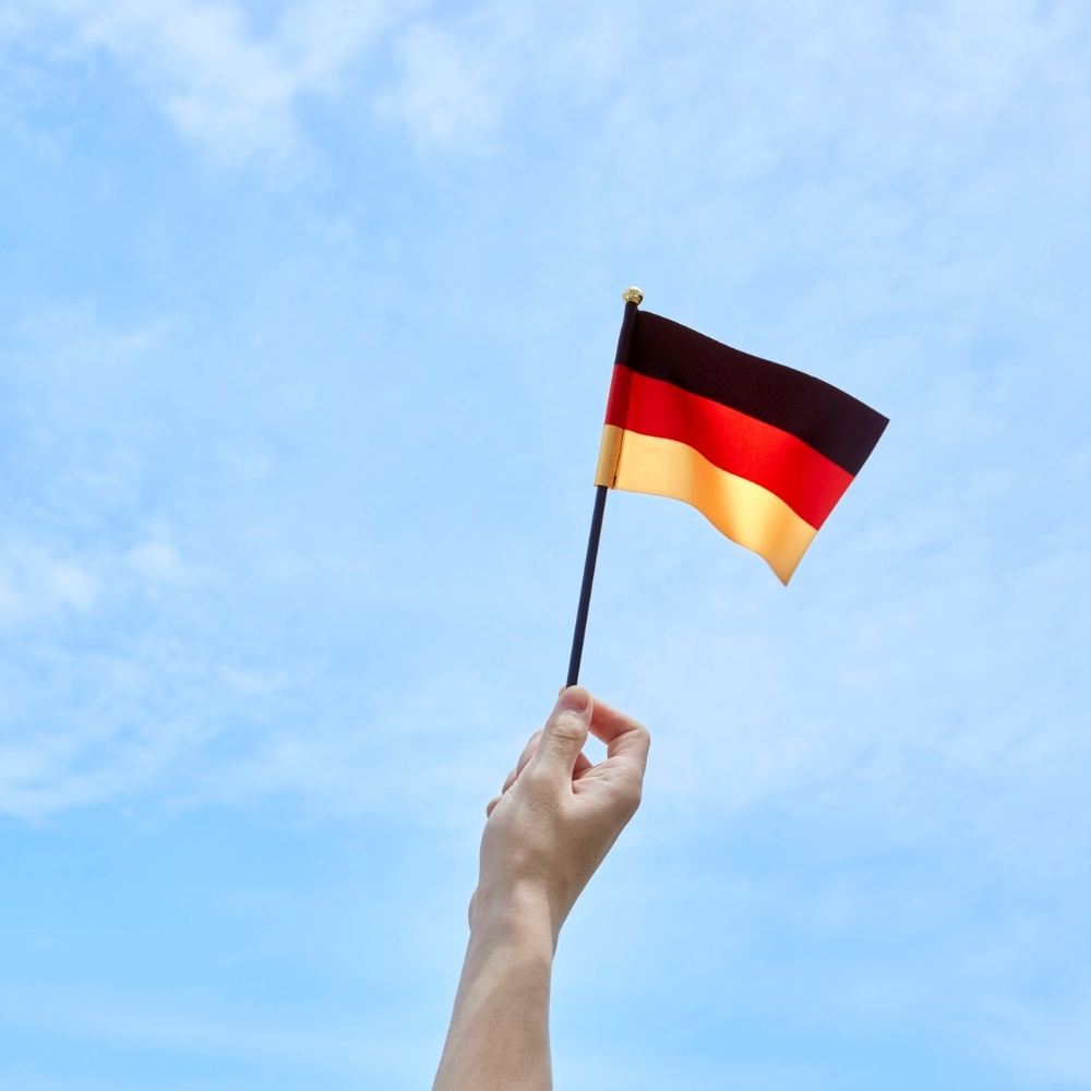 eine hand hält eine kleine deutsche fahne in die luft - sie weht im wind