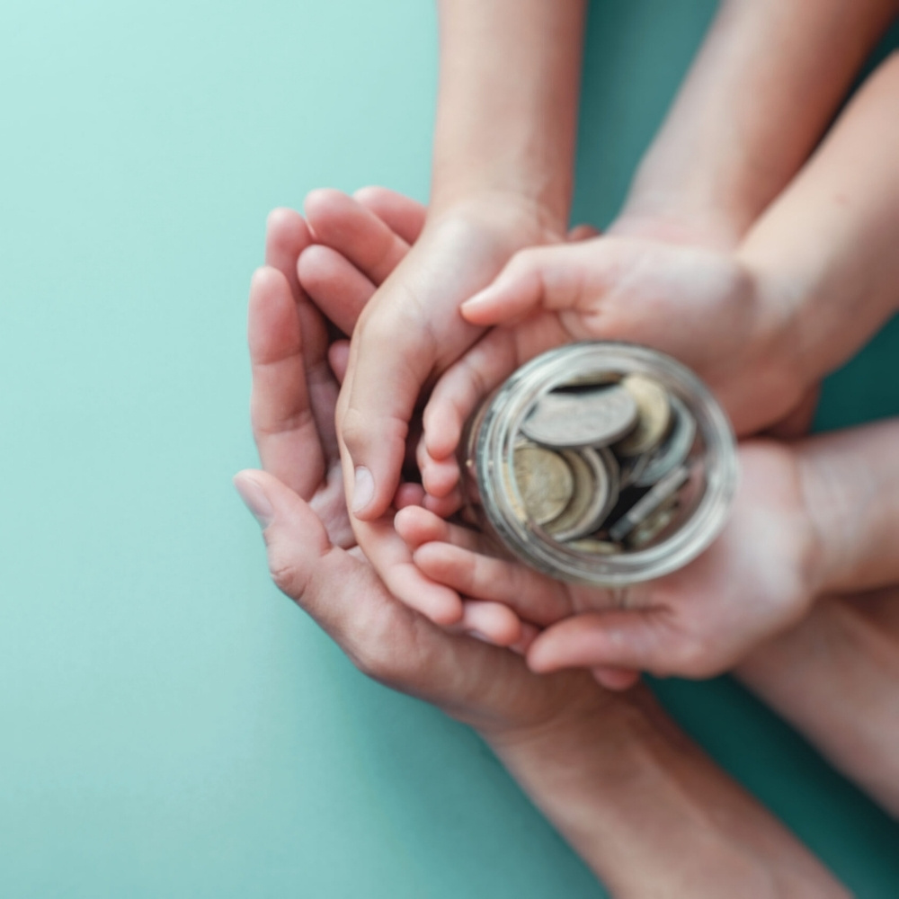 man sieht die hände einer 3köpfigen familie die alle zusammen ein glas mit kleingeld halten