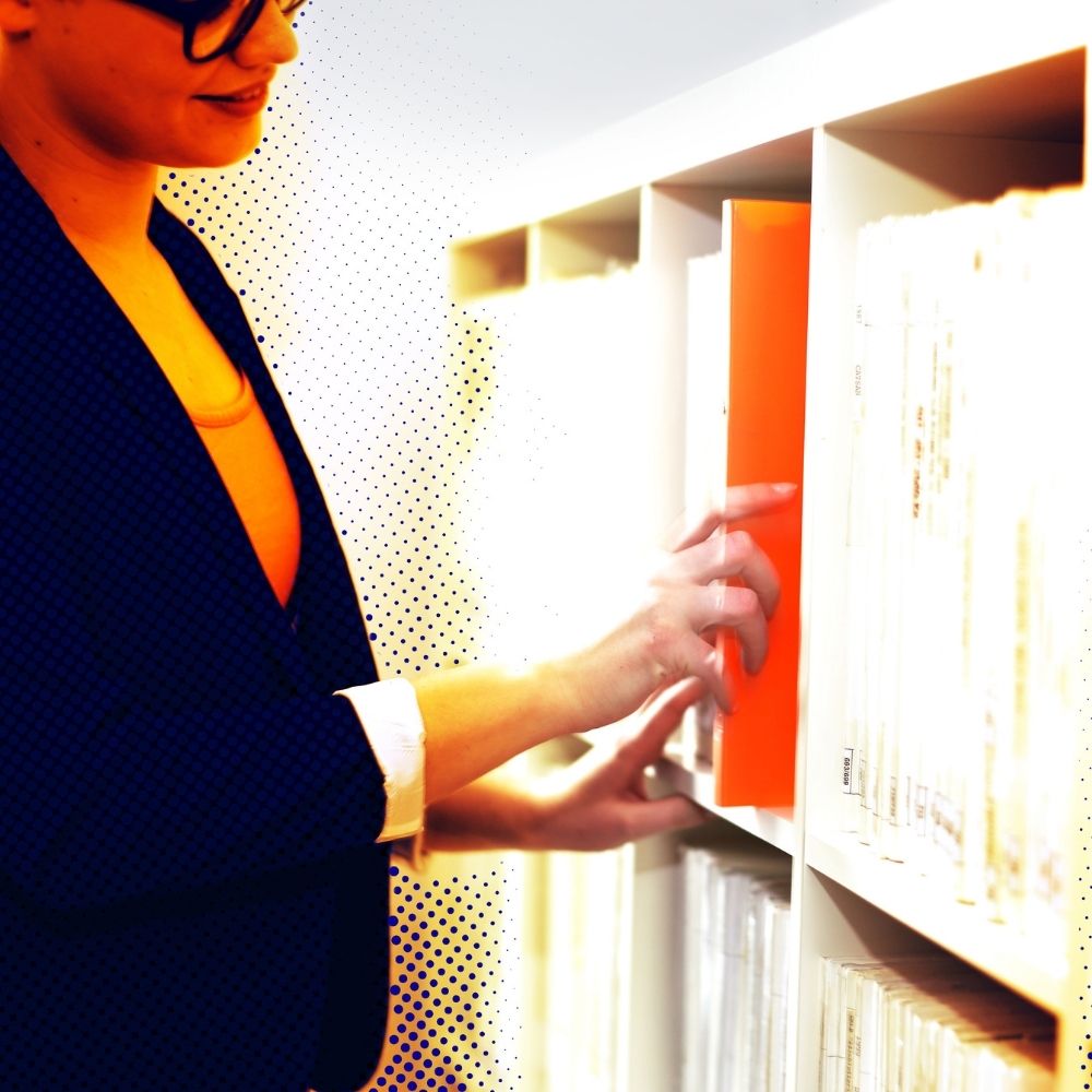 person nimmt einen orangefarbenen ordner aus einem regal